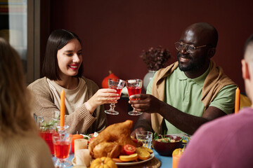 Caucasian woman and black man clinking glasses together sitting at festive thanksgiving table