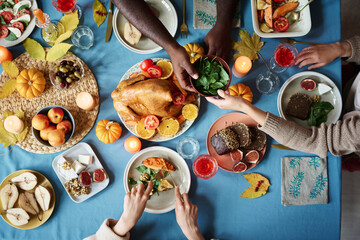 People sharing dinner at fully arranger thanksgiving table full of festive dishes - obrazy, fototapety, plakaty