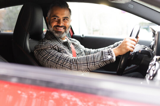 Smiling Indian man driving car while looking away