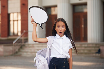 Holding sign with copy space for text. School girl in uniform is outdoors near the building