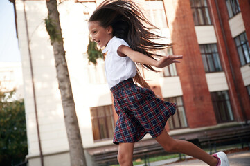 Photo in action, running. School girl in uniform is outdoors near the building