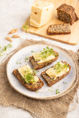 Grain bread sandwiches with cheese and watercress microgreen on gray concrete, side view, close up.