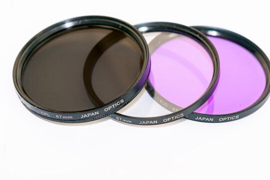 Three filters for dslr photography camera. A CPL "circular polarizer linear" a UV "neutral transparent glass" and a FLD "fluorescent light day" set up on white background. "Japan optics" inscriptions.