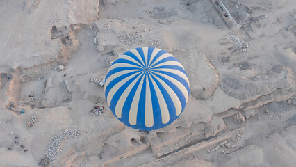 Hot air balloon flying over 
 Hatshepsut Temple at sunrise in Valley of the Kings and red cliffs...