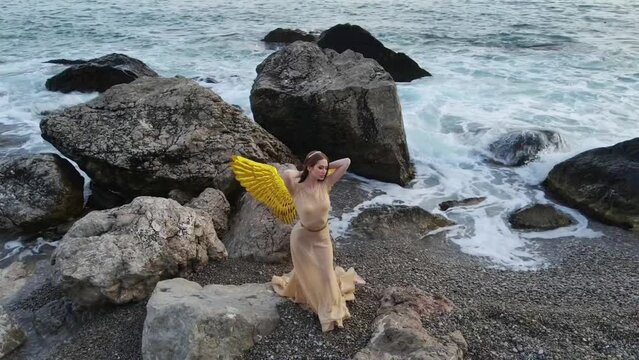 Young beautiful woman fallen angel stands on sea beach enjoy nature. costume bird gold wings.