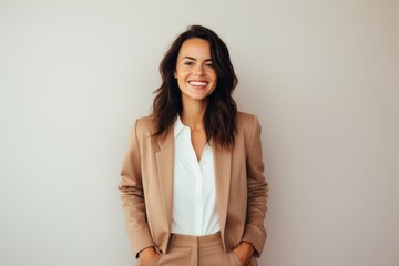 Obraz premium Portrait of a smiling woman in her 30s dressed in a stylish blazer against a minimalist or empty room background. AI Generation