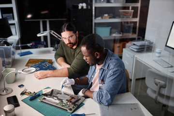 Portrait of two men fixing computers and electronics in tech repair shop, copy space