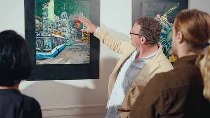 Senior male tour guide pointing at artwork on the wall and speaking about it in front of group of gallery visitors