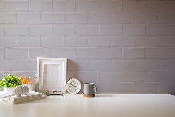Home office interior. Picture frame, coffee cup, notebook and pencil holder on white table against...