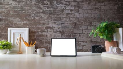 Modern workspace with a tablet computer, pot plant, notebook and coffee cup on white desk. Blank...