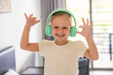 Portrait of little girl listening to the music with kids headphones and dancing at home in happy...