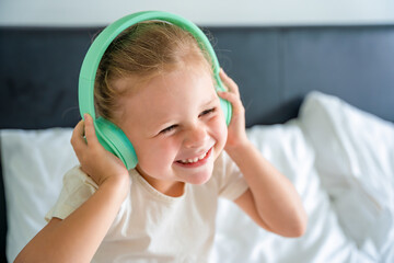 Smiling little girl emotional enjoying music using green kids headphones 