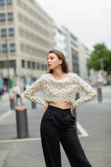 trendy young woman posing in lace top and high waist pants standing on street in Berlin, Germany