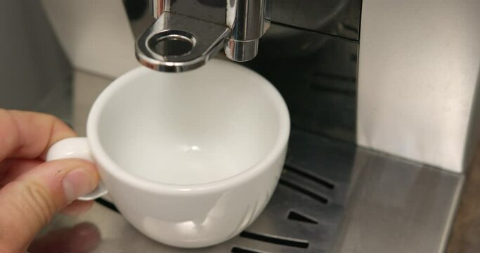 Close-up footage of espresso being poured into a coffee cup by the machine, hand placing an empty cup and retrieving the full one
