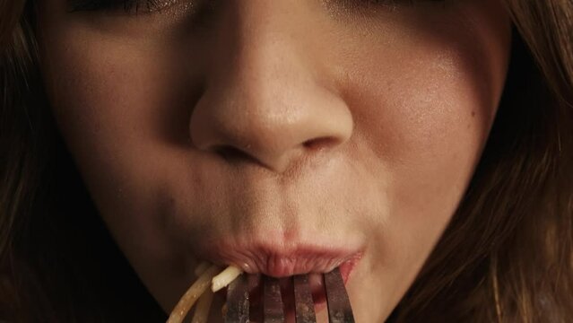 Close up shot of person eating different tasty food. View from a fork, girl puts spaghetti on a fork inside mouth, chewing looking at camera. POV.