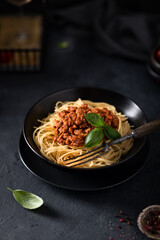 Spaghetti bolognese in a black bowl on dark background, selective focus