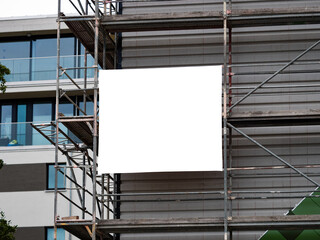 Empty banner on a construction site template. White copy space for a company logo or information of the building. The advertisement is mounted to the scaffolding on the exterior. - obrazy, fototapety, plakaty