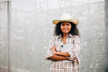 Portrait of a young and successful greenhouse owner wearing a checked shirt and apron standing with...