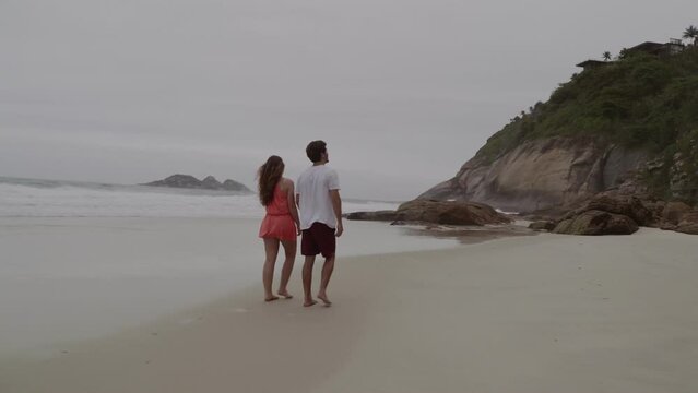 Casal conversando, caminhando pela praia. Visao traseira. Cinematico 4k.