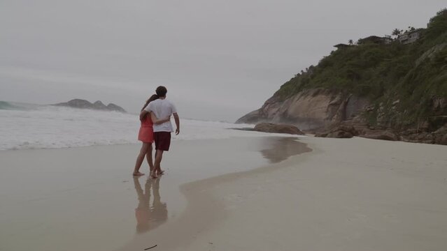 Couple talking, walking hugging along the beach. Rear view. Cinematic 4k.
