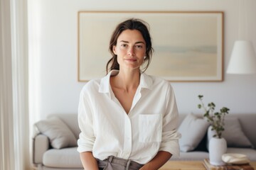 Obraz premium Portrait of a content woman in her 30s wearing a simple cotton shirt against a crisp minimalistic living room. AI Generation