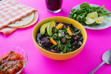 Frijol con puerco - imágenes, fotografías de comida yucateca tradicional, cocina maya ancestral a base de frijol negro y distintos ingredientes cilantro, rábano, cebolla, chile en fondo de color.