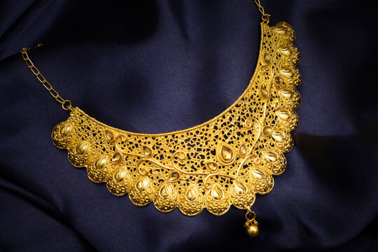 Indian traditional gold jewellery of a Hindu Married woman called as ganthan or choker, necklace on blue silk background. Creative jewellery product photography.