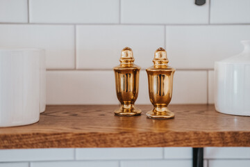 Brass pepper and salt shakers on a wood shelf