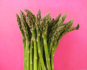 there is a bunch of green raw young asparagus on a pink background. healthy eating. spring...