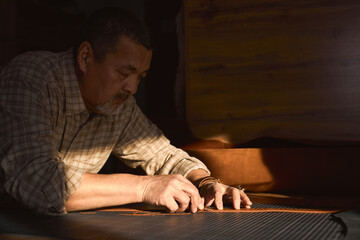 professional artisan makes a new belt, man concentrated on cutting the edges of belt with knife. close up side view photo