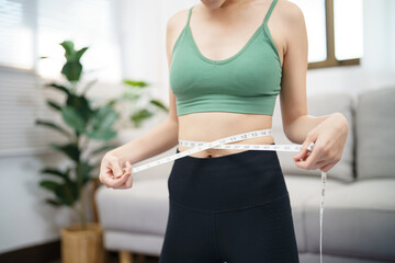 Asian healthy woman dieting Weight loss. Slim woman measuring waist with measure tape after diet at home weight control.
