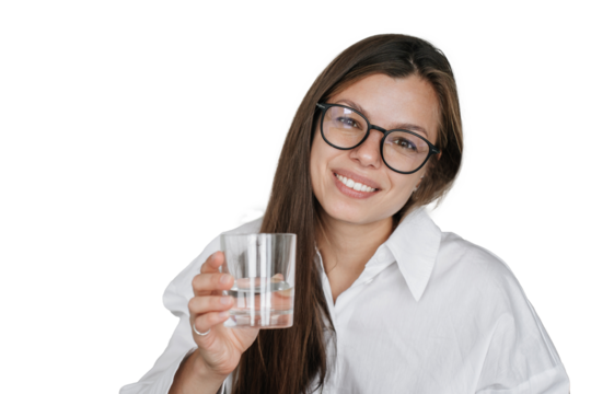 Beautiful Spanish young businesswoman in white shirt and glasses holds glass of water, toothy smiles looks at camera. Pretty brunette Italian woman offers pure water against transparent background
