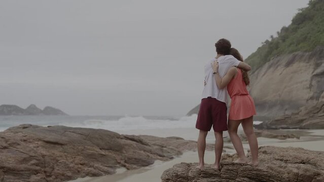 Young couple, hugging, talking, standing on a rock at the beach. Cinematic 4k.
