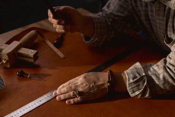 professional craftsman cuts out blanks for sewing bags. close up cropped side view photo.man cutting cloth for belt, bag, tailor repair leather old clothes, accessories