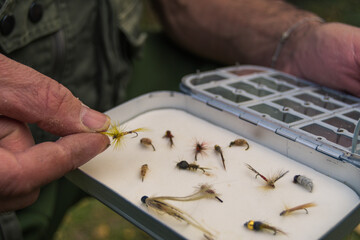 Hand taking a fishing fly out of its case to put it on the rod.