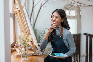 Asian female artist painter on canvas in creative studio as art. Cheerful young asian woman artist...