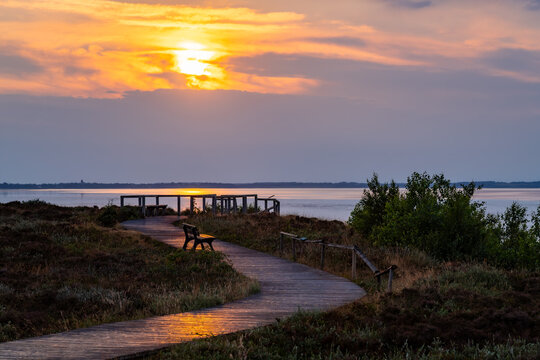 Sunset panorama at Morsum cliff on on Sylt island, North Sea Germany. Idyllic wooden footpath with observation deck and bench in warm evening light. Natural reserve and popular touristic attraction.
