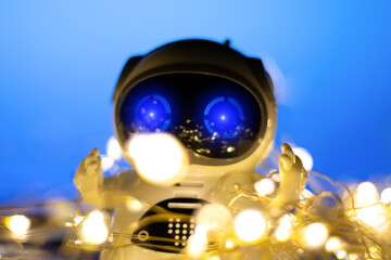 Spread and Development Artificial Intelligence in New Year. Small real robot with garlands on blue background. Modern digital technology concept.