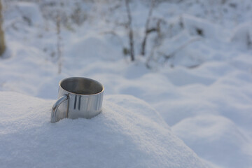 Metal cup with coffee in the snow in the forest at winter