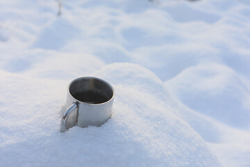 Metal cup with coffee in the snow in the forest at winter