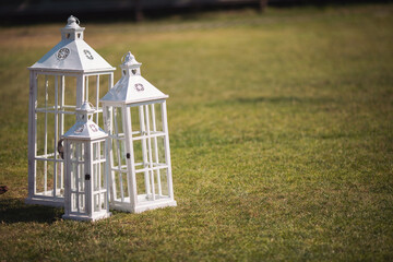 Wedding decor in rustic style.White vintage lamp standing on green grass. Garden decoration. Fancy lanterns stand on green lawn. Beautiful wedding ceremony outdoors. © Cristina