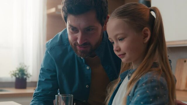 Caucasian father help online task internet homework little girl pupil school child daughter together e-learning studying knowledge distant education study learning using computer laptop at kitchen