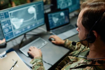 Focus on head of young military officer with headset sitting in front of computer screen with...