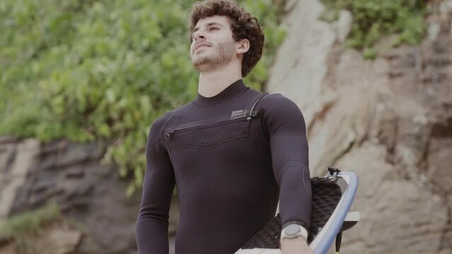 Jovem na praia, concentrado, aplicando parafina na prancha de surf. Cinematico 4k.