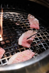 Hand using tongs to pick up wagyu beef on hot charcoal Asian BBQ food style, Grilled Beef meat on the charcoal stove, Korean and Japanese BBQ style.
