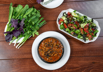Vegetable salad in a bowl and meat with sauce in pan on a wooden table, top view