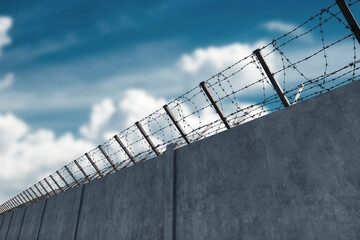 Concrete wall with barbed wire against blue sky. Concept border, prisons, refugees, loneliness....