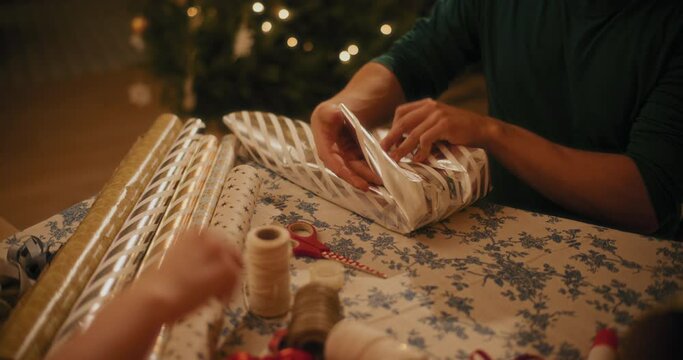 Man wrapping gift paper on box at table