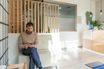 A patient looking at his mobile phone while waiting in the dentist's waiting room.