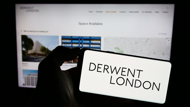 Stuttgart, Germany - 12-08-2023: Person holding smartphone with logo of British real estate company Derwent London plc in front of website. Focus on phone display.